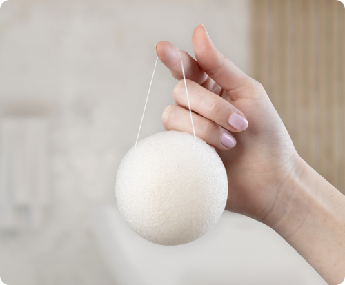White konjac facial sponge hanging from a finger against a neutral background