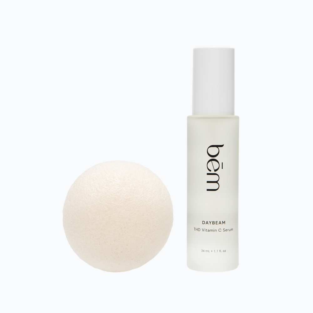 Bēm's Daybeam serum bottle and a round facial sponge on a neutral background