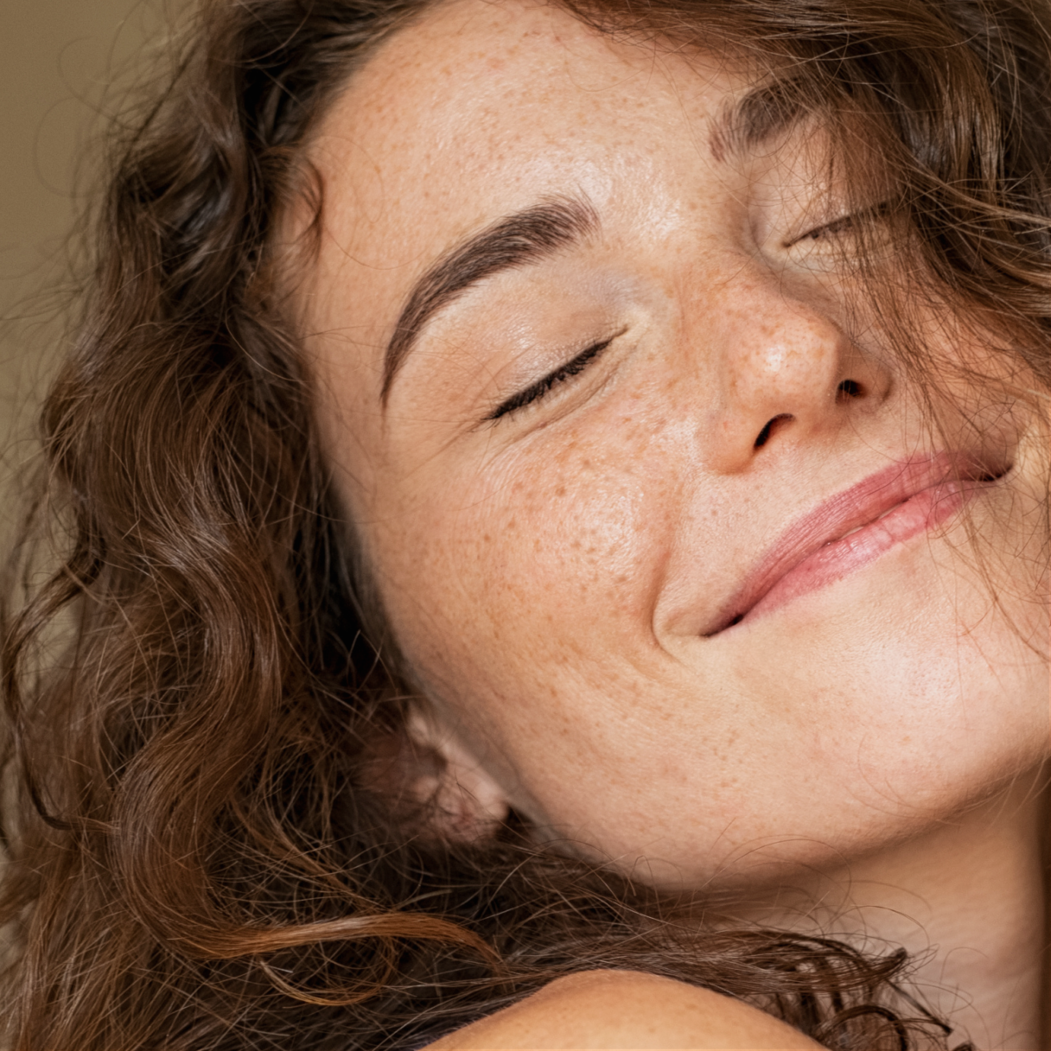 Close-up of a woman with closed eyes and a soft expression and glowing skin.