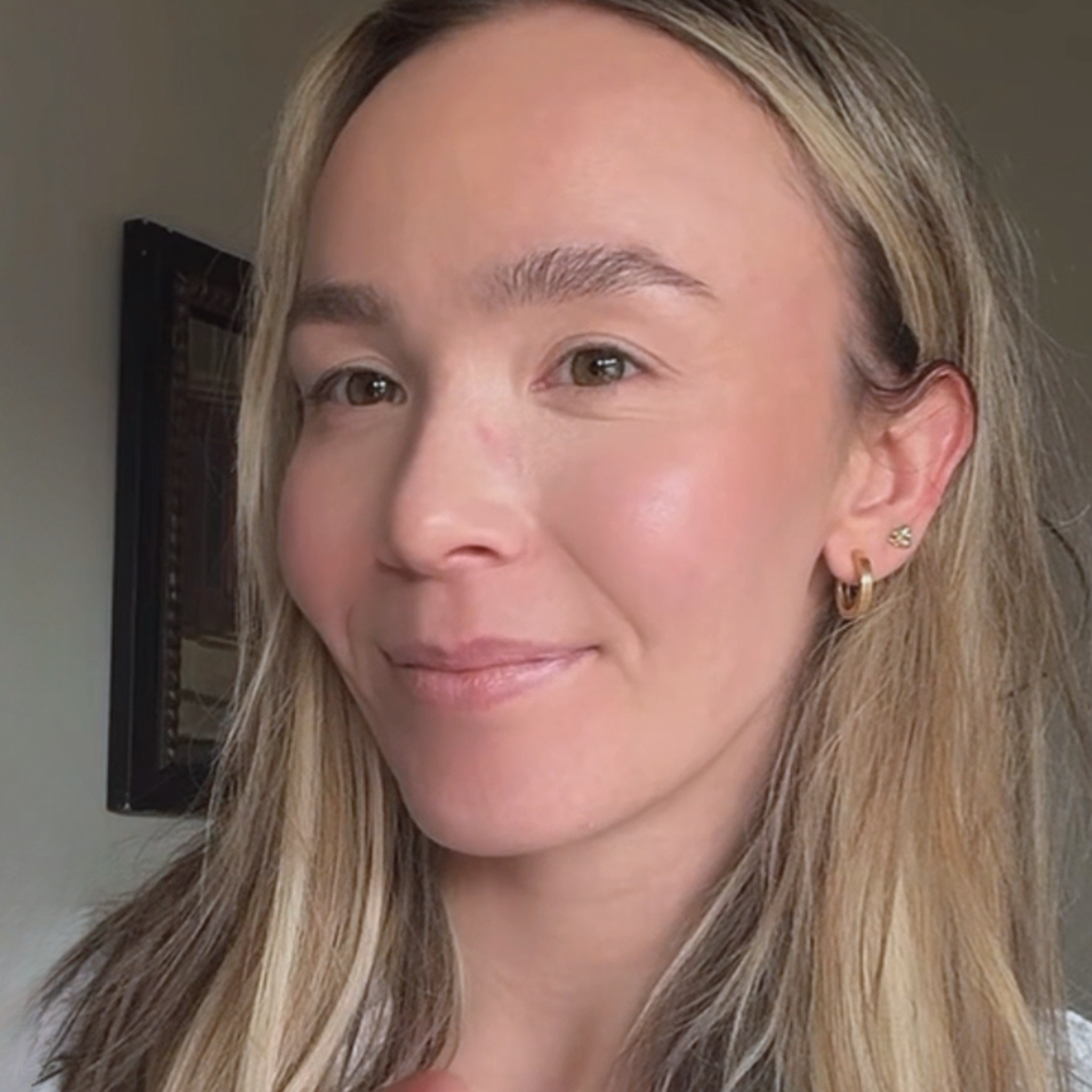 Close-up of a woman with blonde hair and earrings against a neutral background